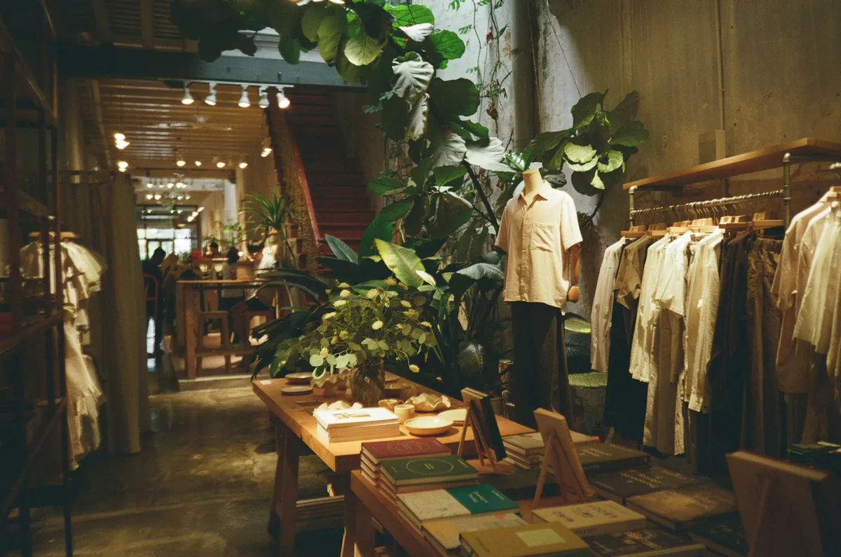 Boutique de prêt-à-porter en lin, tables en bois, grandes plantes vertes et escalier au fond de la salle