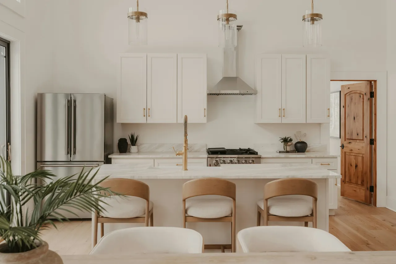 Cuisine blanche lumineuse avec îlot en marbre, tabourets en bois clair et suspensions en verre